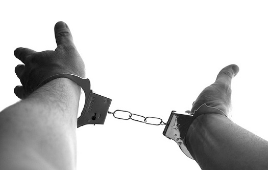 a picture of hands extended above the head locked in handcuffs
