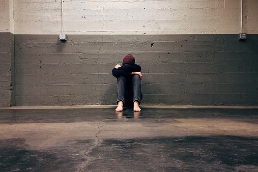 a picture of a lonely man, sitting on the floor against a brick wall