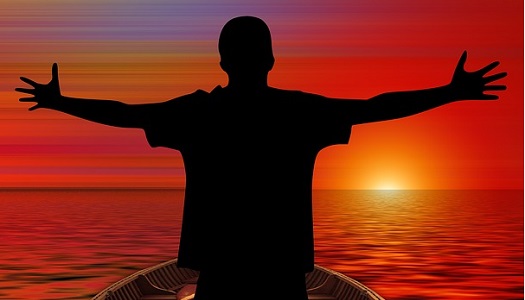 a silhouette of a man standing in a rowboat with his hands stretching toward the setting sun